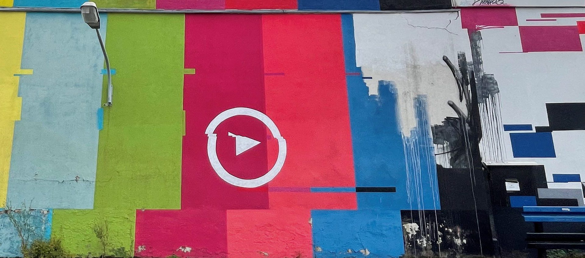 Farbiges Streifen-Wandbild mit Play-Symbol an einer Hausfassade